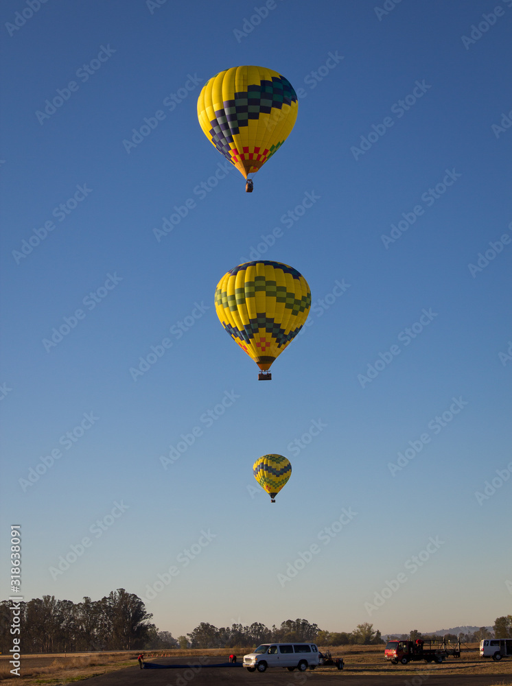 3  yellow and green balloons rising into the blue morning sky together. 
