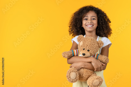 Portrait of smiling african girl hugging teddy bear toy isolated on yellow background
