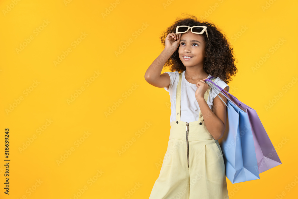 Happy young girl kid holding shopping bag on yellow background in studio Happy young girl kid holding shopping bag on yellow background in studio