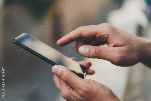 Closeup image of male hands using modern smartphone device outdoor  hipster man typing an sms message via cellphone while walking in urban streets  communication concept