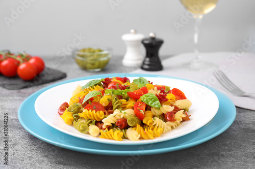 Colorful pasta with basil and tomatoes on grey table