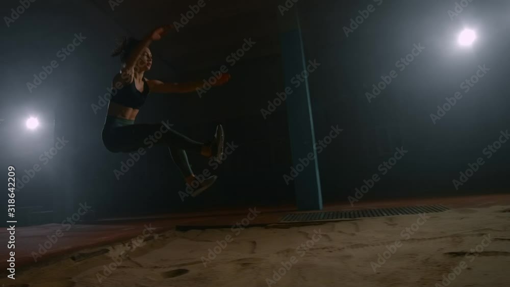 Professional long jumper in slow motion at competitions runs on a treadmill and flies on a dark background in the sand Professional long jumper in slow motion at competitions runs on a treadmill and flies on a dark background in the sand