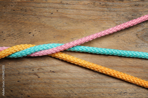Twisted colorful ropes on wooden background, top view. Unity concept