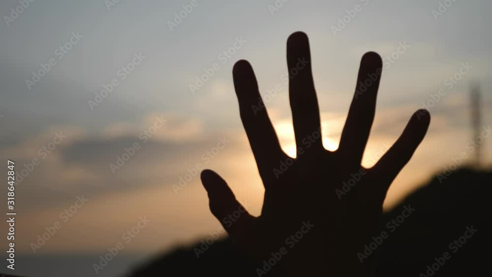 The hand of a man at sunset covers the sun. The man waves his hand The hand of a man at sunset covers the sun. The man waves his hand