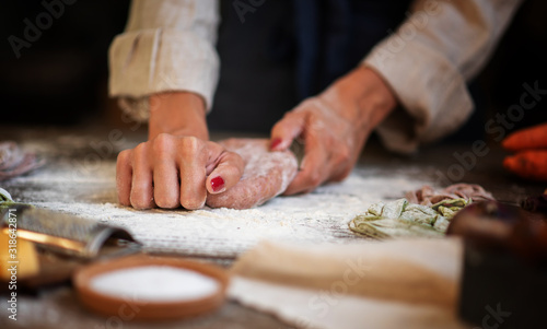 Fresh homemade pasta with pasta ingredients on the dark wooden table top view. Female making homemade pasta with flour and eggs over old wooden table.