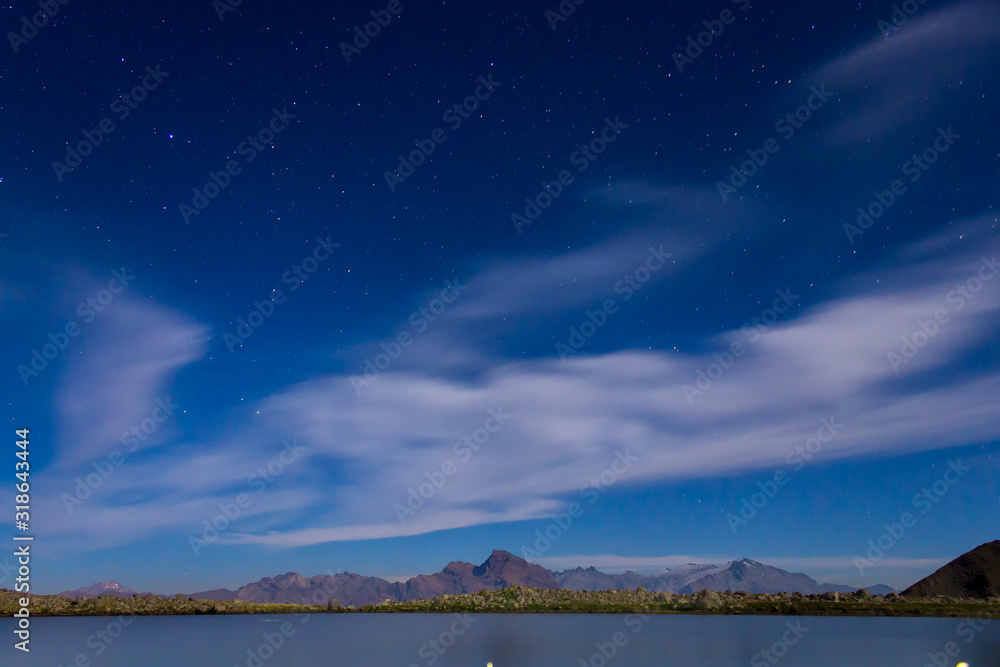 noche de astrofotografia con un cielo parcialmente nublado con vista a Laguna Verde y sus montañas - obrazy, fototapety, plakaty 