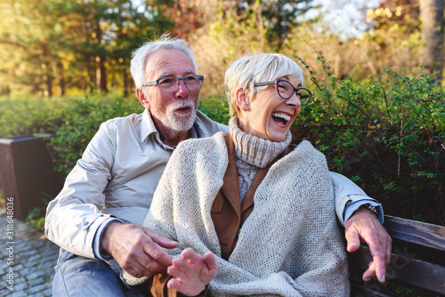 Smiling senior couple sitting on the bench in the park together enjoying retirement