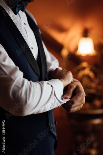 A groom fastens with a cufflink on the cuff of the sleeve of a luxurious white shirt. A man hand wearing a white shirt and cufflinks. Captures the groom cufflinks. Groom in fashionable suit