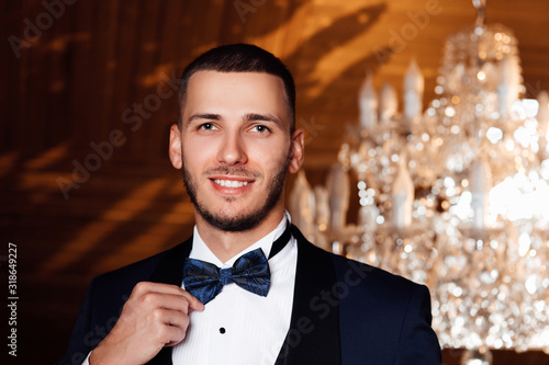 Man's hands straighten a black bow-tie. A groom with beard in a suit, a white shirt and a black bow-tie. Wedding. Details. stylish men's suit. Preparations for the wedding. Fees of the groom.