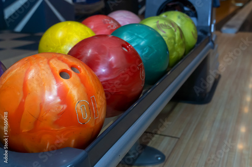 Bowling balls lie in a holder in a line. Colored balls and bowling lane.