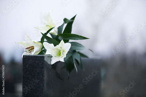 Fototapeta Naklejka Na Ścianę i Meble -  White lilies on black granite tombstone outdoors, space for text. Funeral ceremony