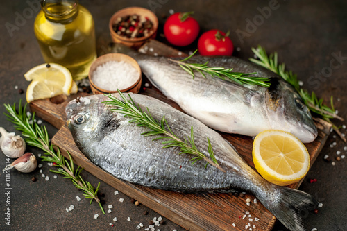 Fresh dorado fish with spices and ingredients tomato, razmorin, sunflower oil, lemon for cooking on a stone background