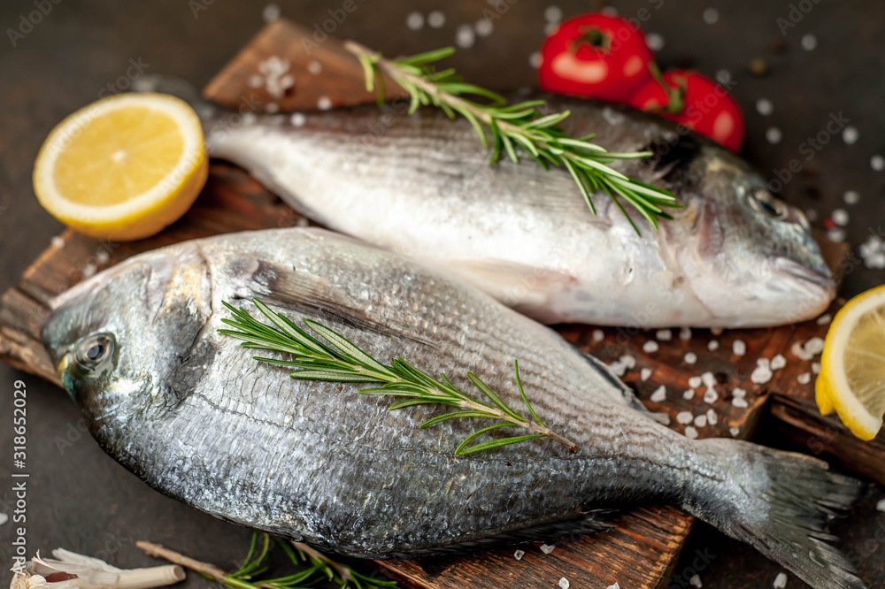 Fresh dorado fish with spices and ingredients tomato, razmorin, sunflower oil, lemon for cooking on a stone background Fresh dorado fish with spices and ingredients tomato, razmorin, sunflower oil, lemon for cooking on a stone background