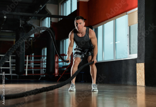 Man working out with battle ropes in modern gym