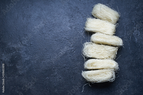  Uncooked rice noodles rolled in nests on dark background. Ingredient of asian cuisine. photo