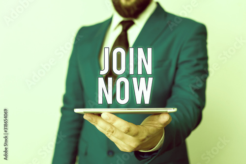 Conceptual hand writing showing Join Now. Concept meaning An invite to a demonstrating or a friend to become a member of the group Businessman in blue suite with a tie holds lap top in hands photo