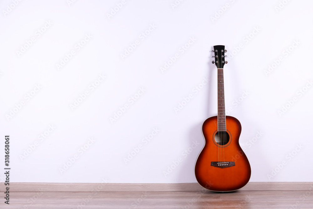 Folk style parlor acoustic guitar over white wall background with a lot of copy space for text. Studio shot of travel size musical instrument. Close up.