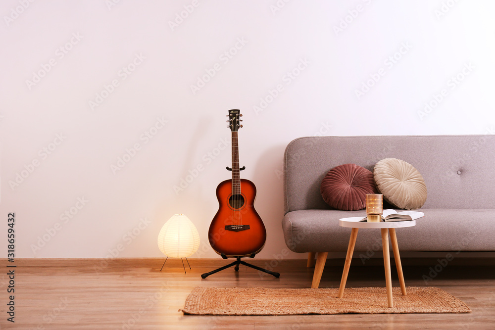 Minimalistic interior design concept. Acoustic guitar on grey textile sofa in spacious room of loft style apartment with wood textured laminated flooring. Background, copy space, close up. - obrazy, fototapety, plakaty 