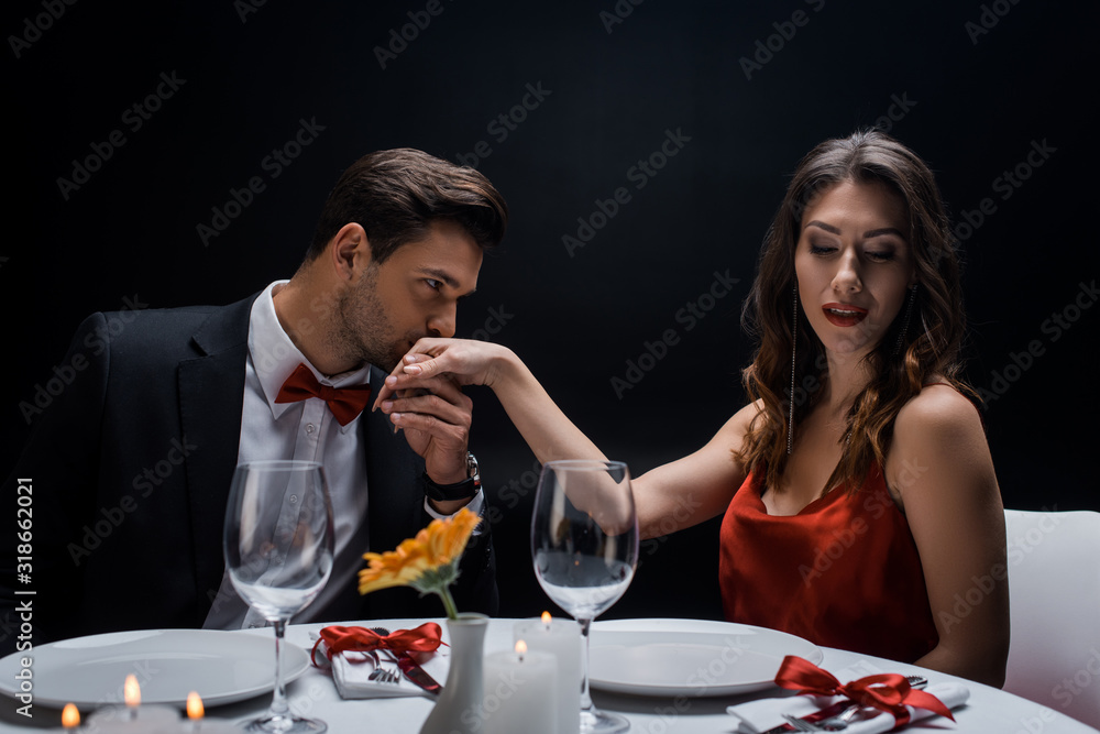 Elegant man kissing hand of attractive woman during romantic dinner isolated on black Elegant man kissing hand of attractive woman during romantic dinner isolated on black