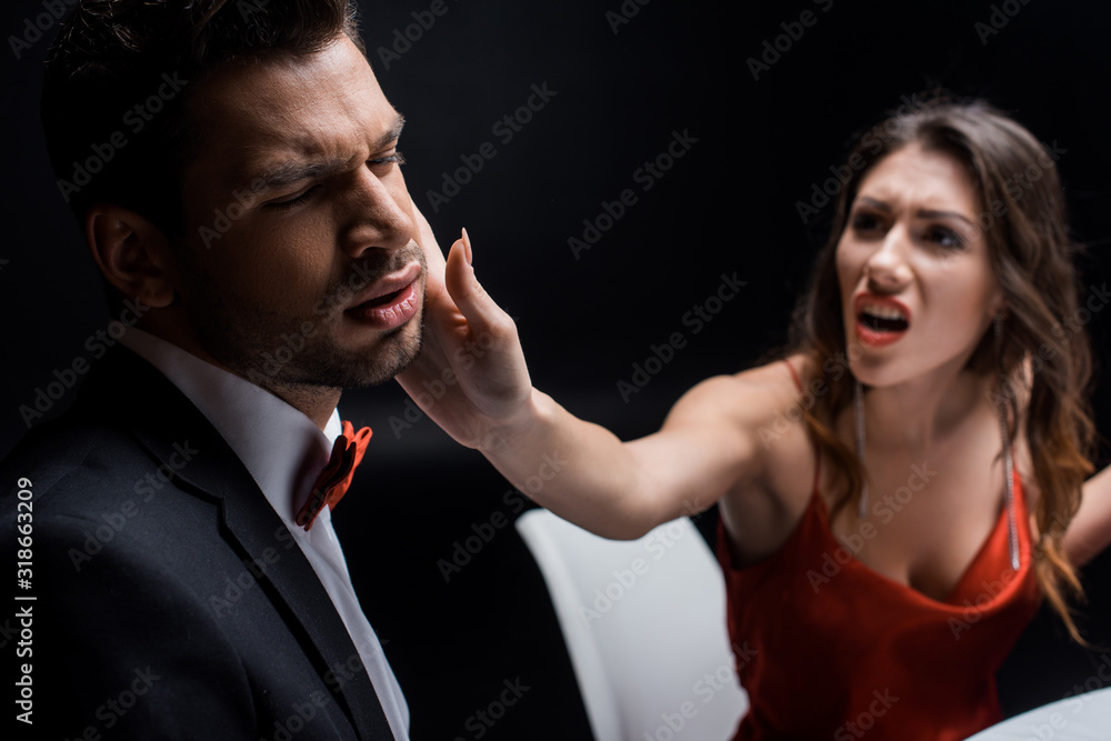 Naklejka premium Selective focus of screaming woman slapping elegant boyfriend at table isolated on black