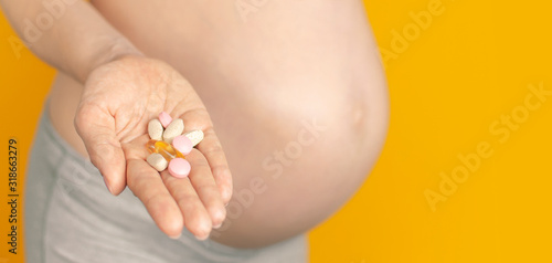 Beautiful young pregnant woman holds vitamins pills tablets in her hand on yellow background selective focus copy space. Pregnant Health Concept, expectation of the child, pregnancy and motherhood