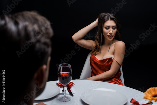 Selective focus of sensual woman touching hair while dining with man isolated on black