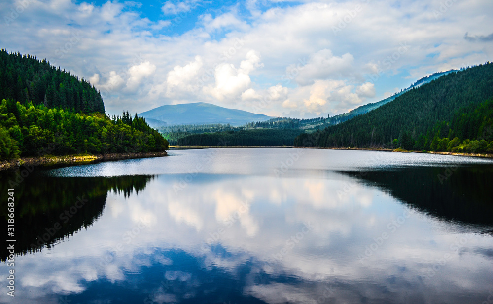 Beautiful Oasa lake between the mountains mirroring the clouds and the sky, Transalpina road, Romania.