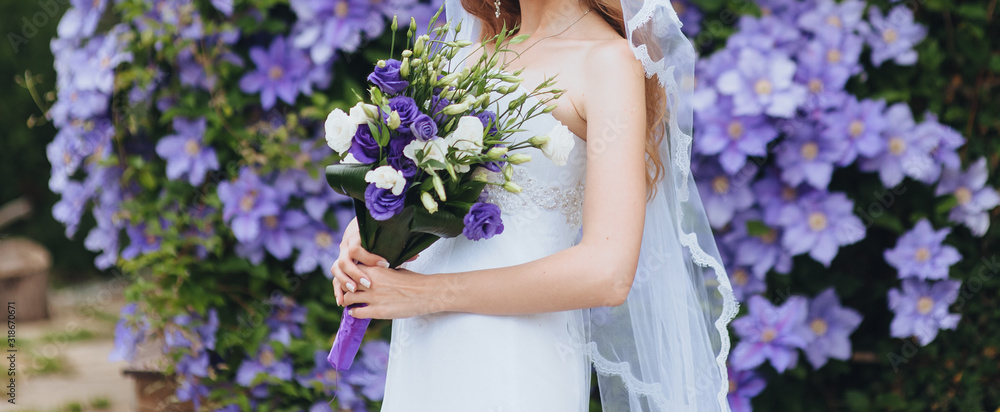 Wedding bouquet of purple and white eustomas close-up in the hands of the bride in a white dress with a veil. Flower portrait in nature. Photography, concept.