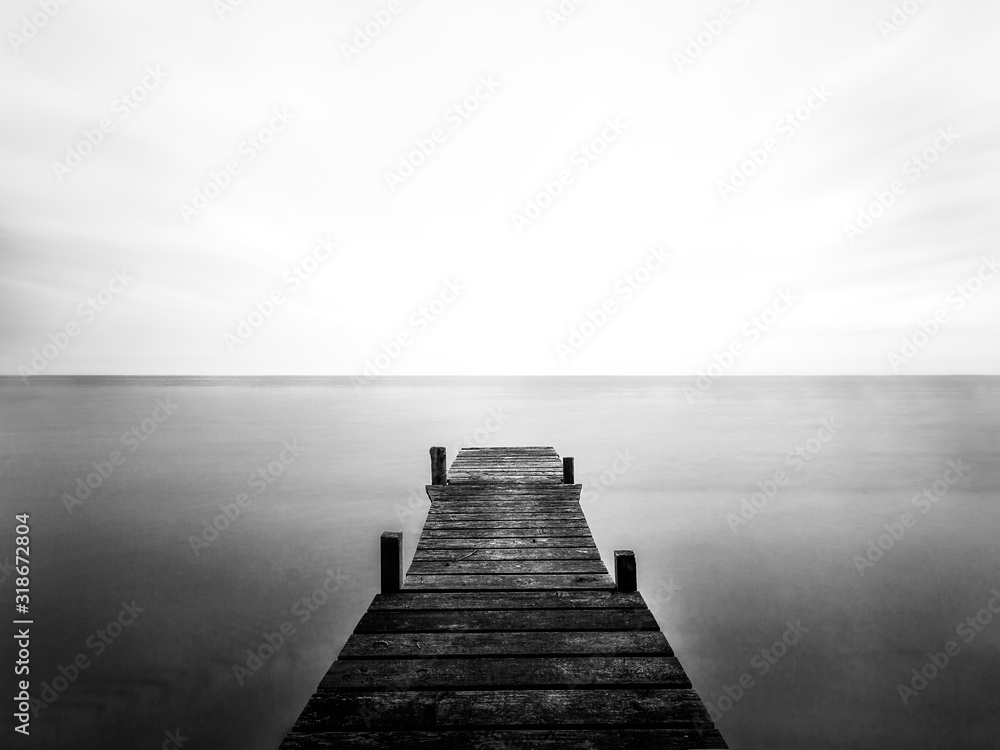 Fototapeta Greyscale of a wooden bridge on the sea under the sunlight and a cloudy sky
