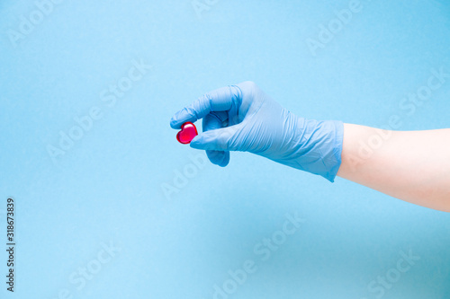 female hand in a blue disposable medical glove holds a small red glass center on a blue background, copy space, cardiology concept, health care and treatment and prevention of heart diseases