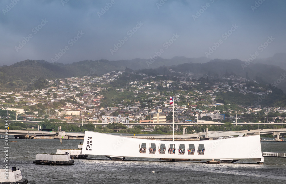Oahu, Hawaii, USA. - January 10, 2020: Pearl Harbor. White USS Arizona Memorial and Ford Island bridge in back. Green Hills with white buildings under rainy blue cloudscape behind.