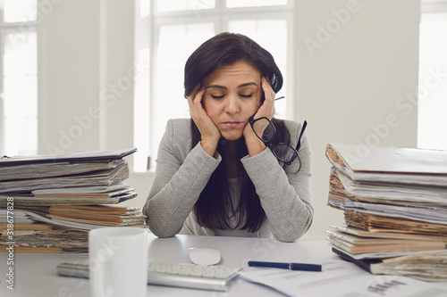 Fotografia Woman brunette businesswoman in glasses with a mountain of documents on the tabl