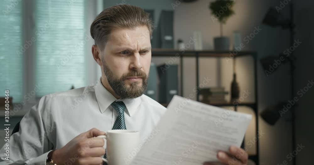 Handsome middle-aged businessman in white shirt and tie checking document and holding cup of coffee Handsome middle-aged businessman in white shirt and tie checking document and holding cup of coffee