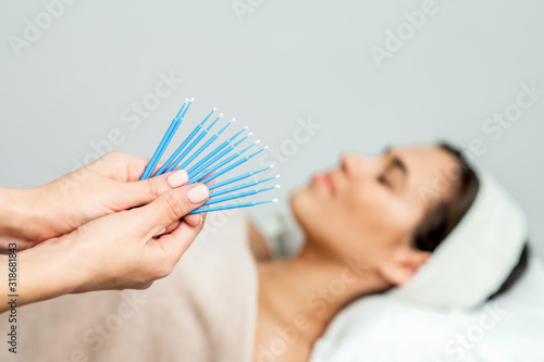 Eyelash extension disposable microbrushes, eyelash cotton swabs in hands on backgrond of patient, close up.