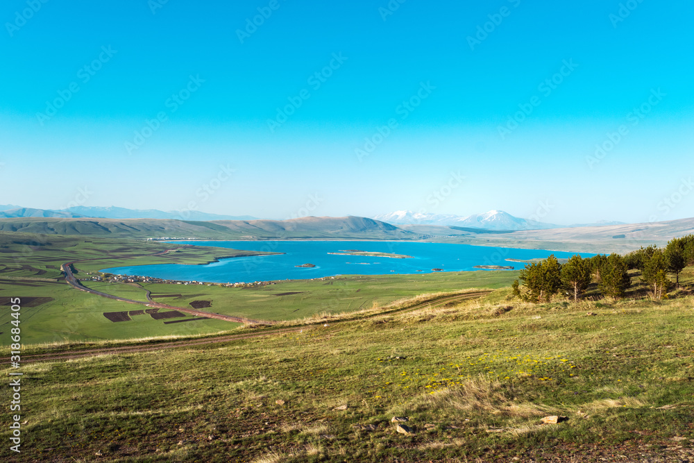 Beautiful landscape. View from the hill overlooking light blue lake water and lush hills in the background. Spring theme with clear sky.