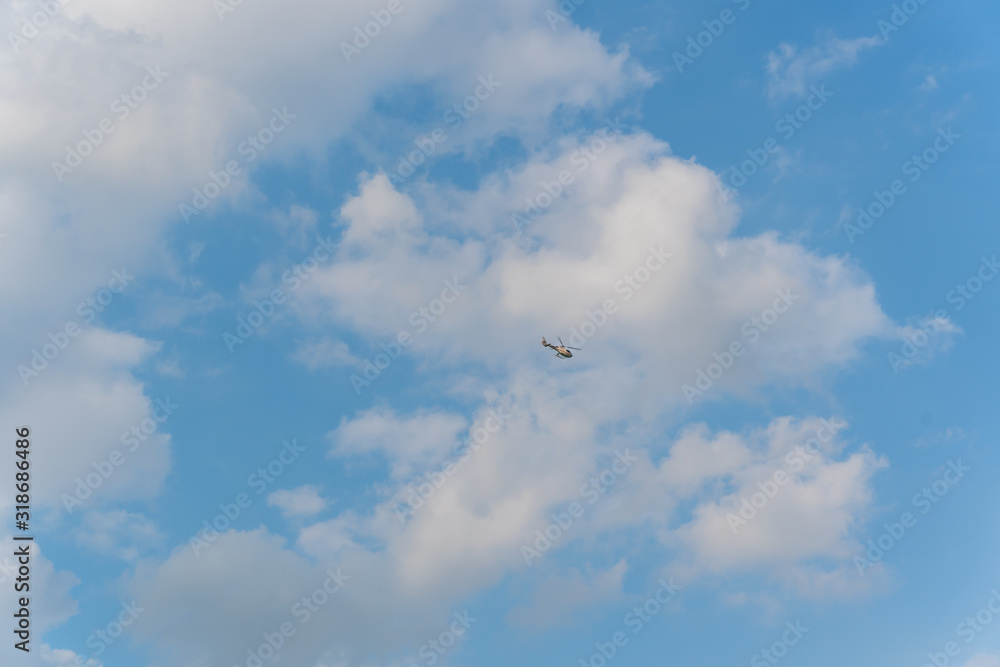 Small helicopter in the sky, among white clouds. Shot at bright sunny day.