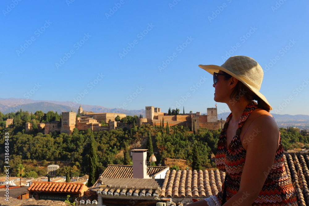 A young tourist woman with a summer hat on her head, watching the Alhambra (Granada) from the distance