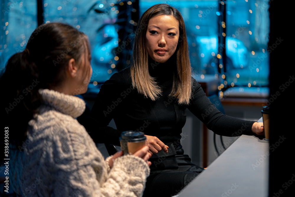 Asian Young Woman Attentively Listening Her Friend In Oversize Sweater And Drinking Coffee.