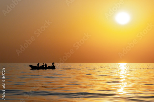 Fototapeta Naklejka Na Ścianę i Meble -  Silhouettes of fishermen against a bright sunset with a large yellow sun under the surface of the sea. Beautiful sunset over the sea