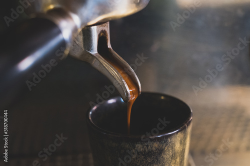 Nahaufnahme eines leckeren braunen Espressos, der frisch durch eine Siebträger Kaffeemaschine in eine Espressotasse läuft photo