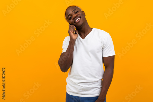 handsome smiling dark-skinned man in a white T-shirt talking on the phone on an orange studio background