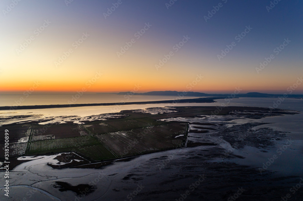 Aerial view of the Sado Estuary near the village of Carrasqueira, with a rice plantation, the Troia Peninsula and the Arrabida Mountain on the background at sunset, in Portugal.