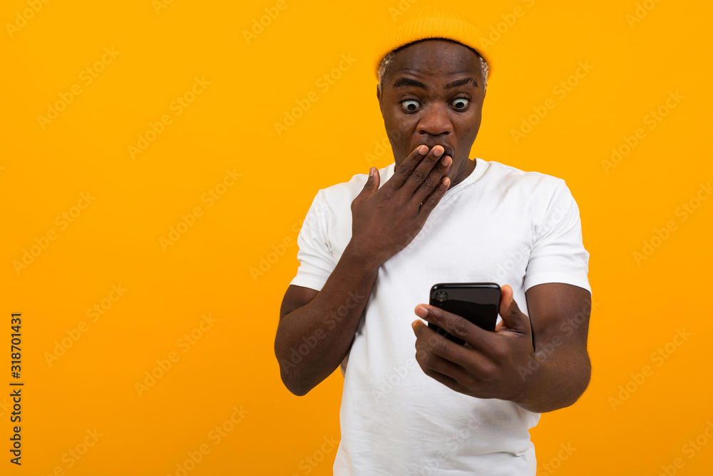 black man looks in surprise on the phone on an orange background black man looks in surprise on the phone on an orange background