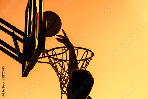 Silhouetted unrecognized person basketball player jumping high reaches target scoring at sunset.. Target achiement concept. photo