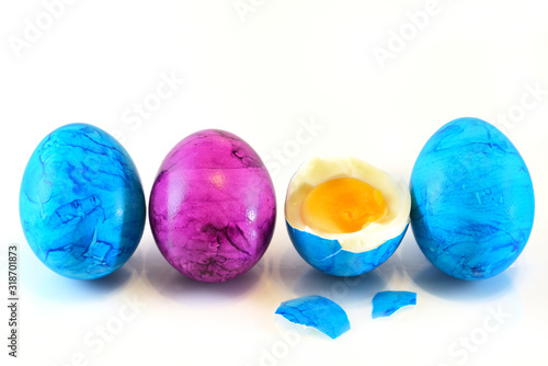 Four marbled colored, blue and pink Easter eggs stand side by side in a row against a white background. One egg is open and you can see the inside.