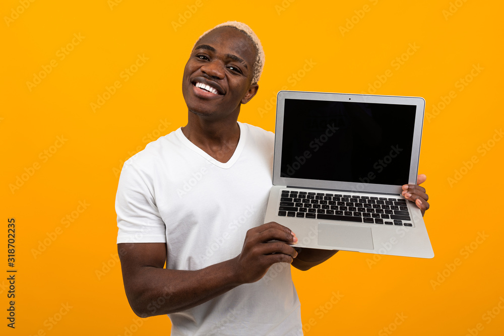 handsome african man with pretty smile holds laptop wireless computer with mock up on yellow background handsome african man with pretty smile holds laptop wireless computer with mock up on yellow background