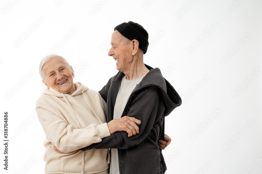 Happy smiling positive pencioner couple in hoodies hugging, stylish old man and woman isolated over white background, copyspace for your text Happy smiling positive pencioner couple in hoodies hugging, stylish old man and woman isolated over white background, copyspace for your text