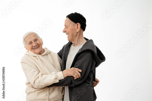 Happy smiling positive pencioner couple in hoodies hugging, stylish old man and woman isolated over white background, copyspace for your text