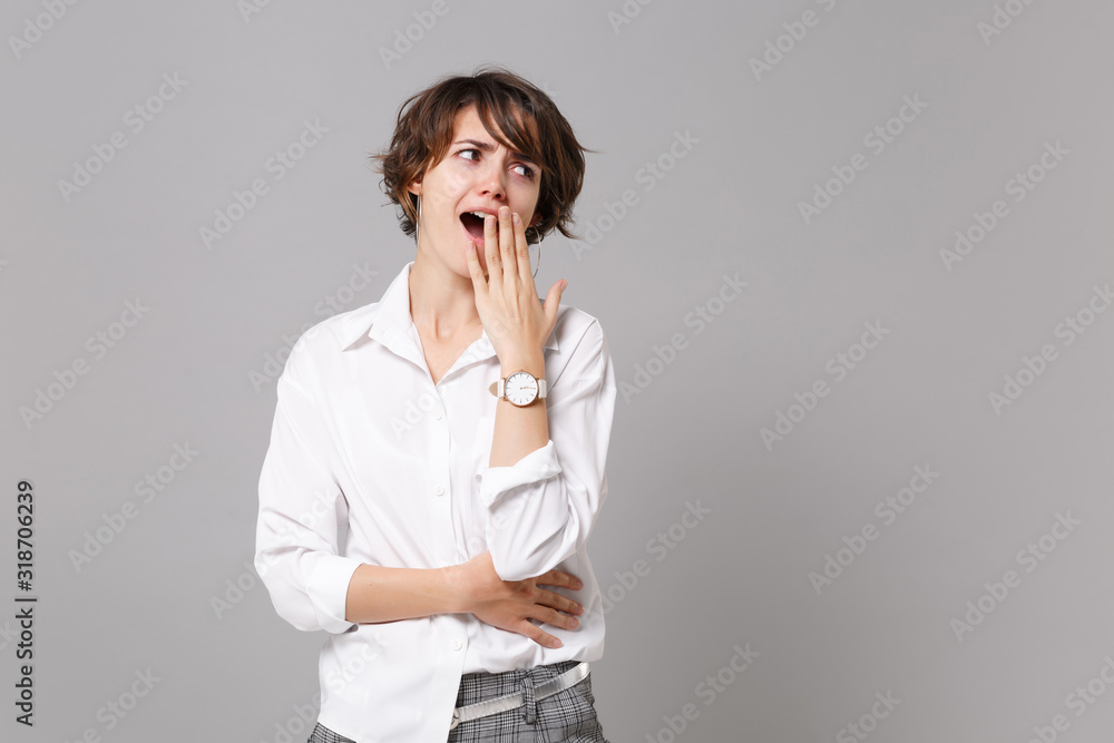 Amazed tired young business woman in white shirt posing isolated on grey background studio portrait. Achievement career wealth business concept. Mock up copy space. Yawning, covering mouth with hand. Amazed tired young business woman in white shirt posing isolated on grey background studio portrait. Achievement career wealth business concept. Mock up copy space. Yawning, covering mouth with hand.
