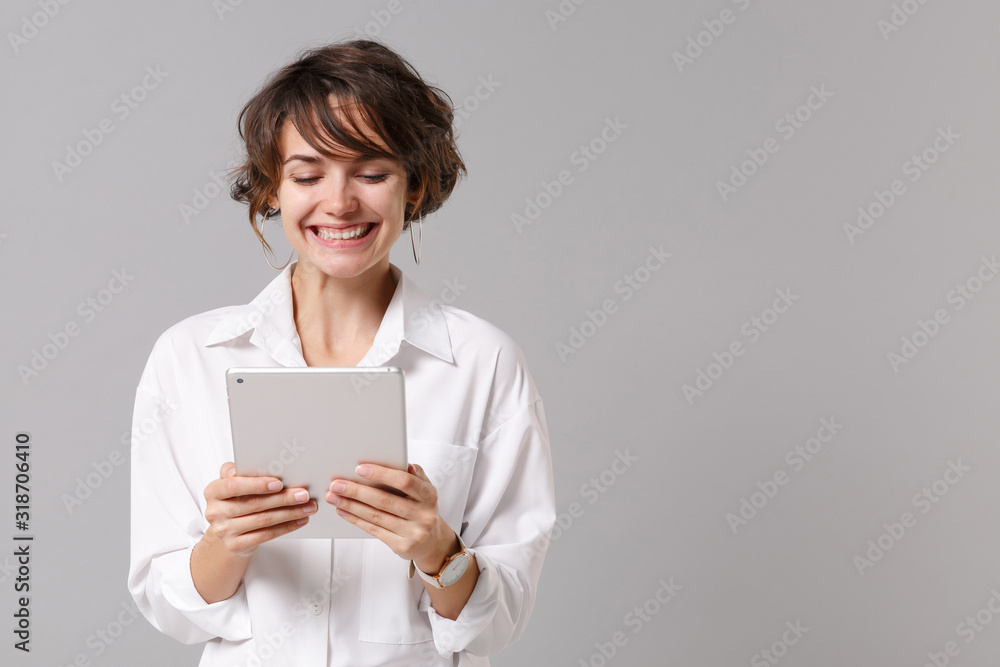 Pretty young business woman in white shirt posing isolated on grey wall background studio portrait. Achievement career wealth business concept. Mock up copy space. Holding, using tablet pc computer. Pretty young business woman in white shirt posing isolated on grey wall background studio portrait. Achievement career wealth business concept. Mock up copy space. Holding, using tablet pc computer.